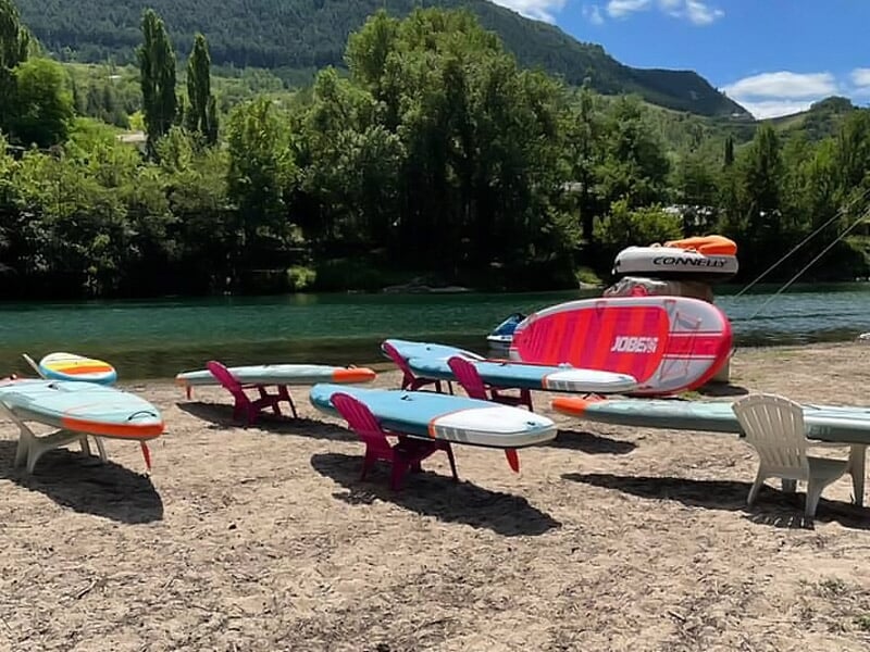 Planches de stand-up paddle posées sur des supports sur une plage au bord d'une rivière.