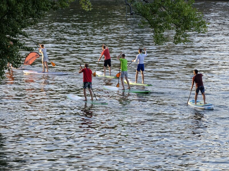 Groupe de personnes debout sur des planches de stand-up paddle pagayant sur une rivière.