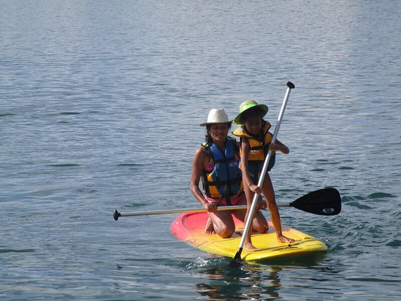 Une femme et un enfant sur un stand-up paddle jaune et rouge pagayant ensemble sur un lac.