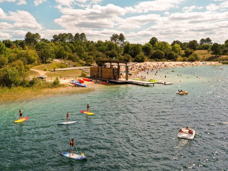 Vue aérienne d'un lac avec plusieurs personnes sur des stand-up paddles et des bateaux près d'une plage.