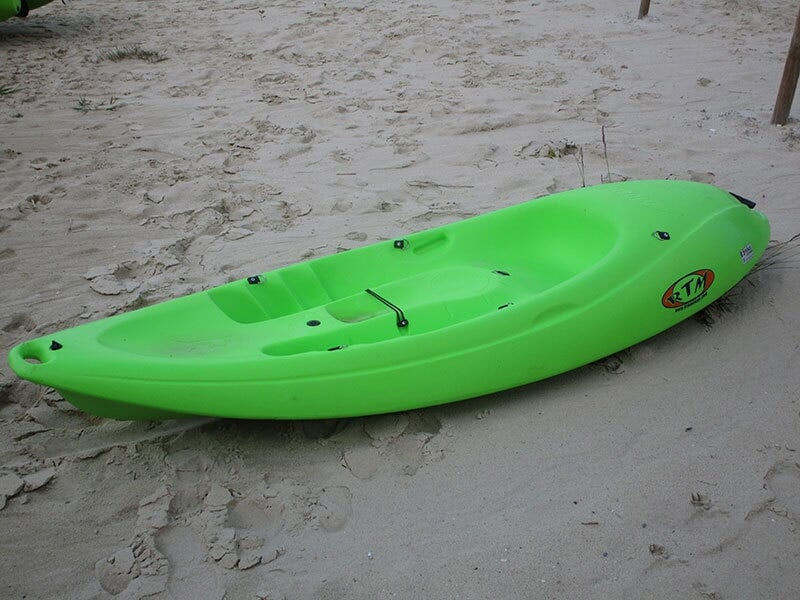 Kayak vert posé sur le sable d'une plage, prêt à être utilisé pour une sortie sur l'eau.