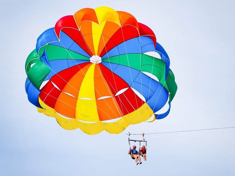 Personnes en parachute ascensionnel sous un parachute multicolore vibrant au-dessus de la mer claire.