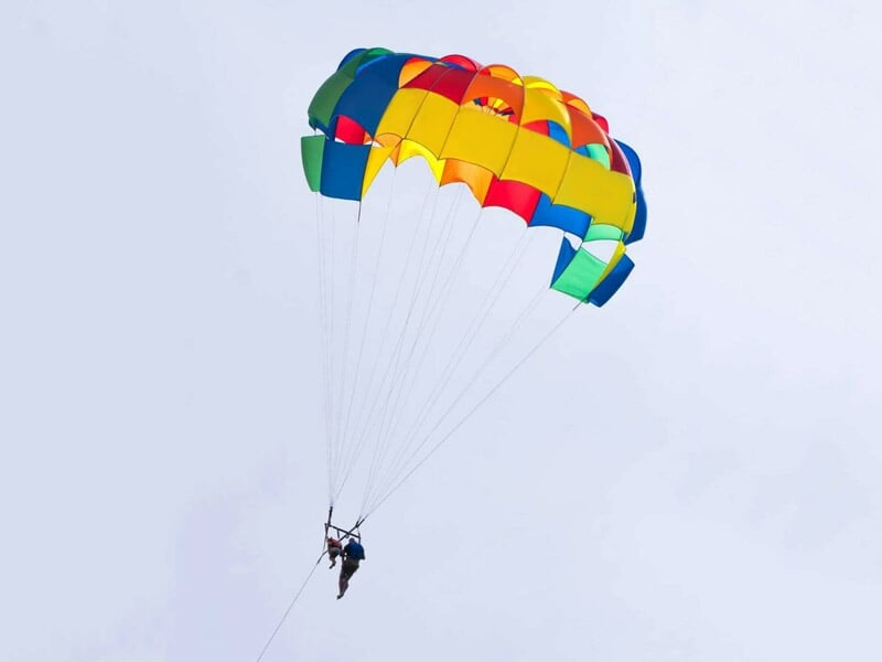 Individu en parachute ascensionnel avec un parachute coloré, suspendu dans le ciel bleu clair.