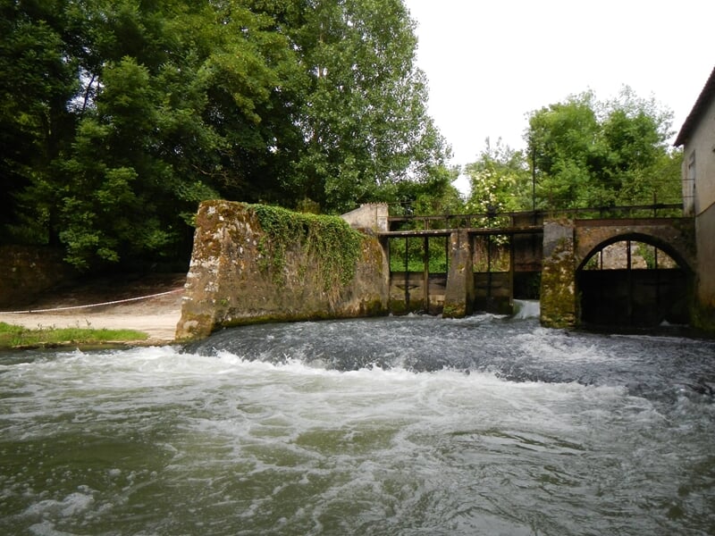 Vue d'une rivière avec un ancien barrage en pierre et un déversoir où l'eau s'écoule vigoureusement.