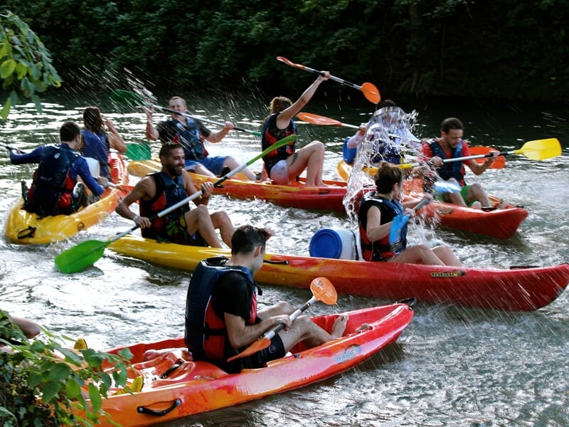 Groupe de personnes en kayaks colorés s'amusant sur une rivière, éclaboussant l'eau joyeusement.