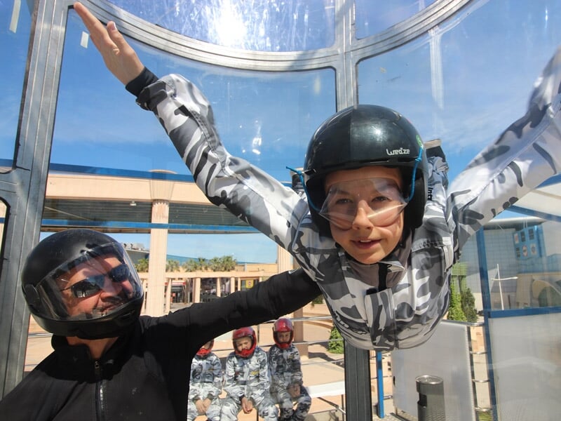 Jeune fille en combinaison camouflage et casque noir s'exerce au simulateur de chute libre avec un moniteur à Montpellier.