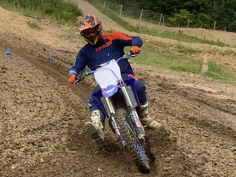 Motocycliste en combinaison bleue et orange, avec un casque orange, prenant un virage serré sur une moto bleue tout-terrain sur un terrain accidenté.
