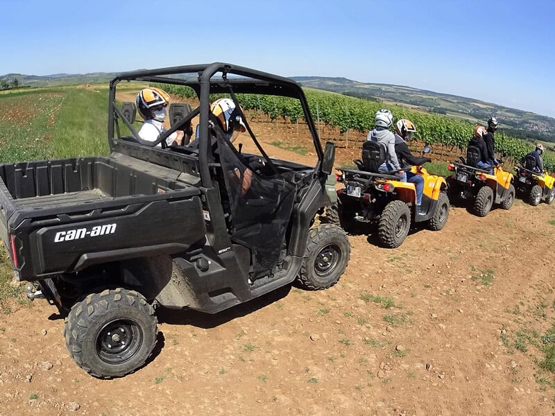 Groupe de personnes en quad et buggy tout terrain sur un chemin de terre en pleine campagne sous un ciel bleu.