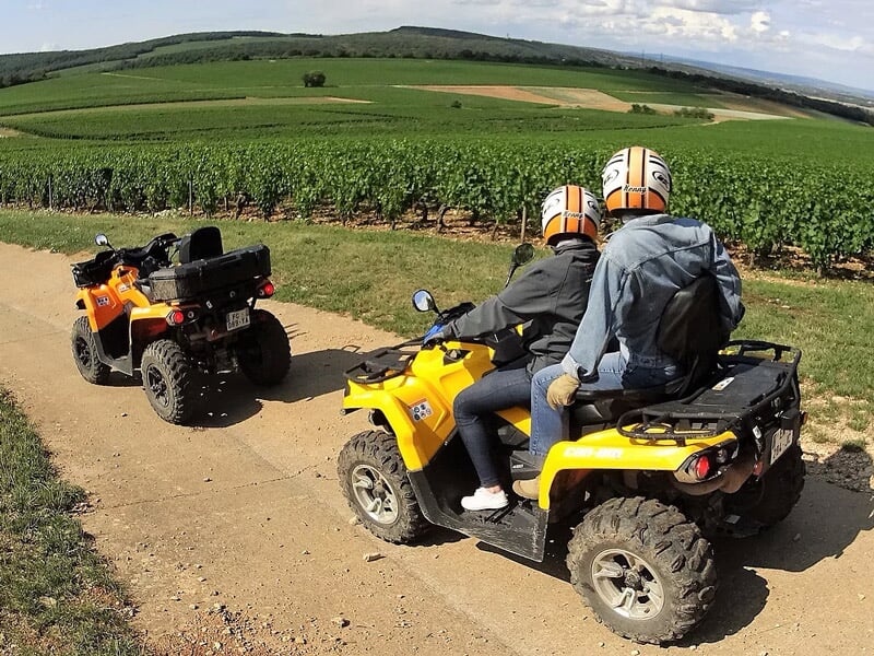 Deux personnes en quad jaune roulant sur un chemin entouré de vignes sous un ciel partiellement nuageux.
