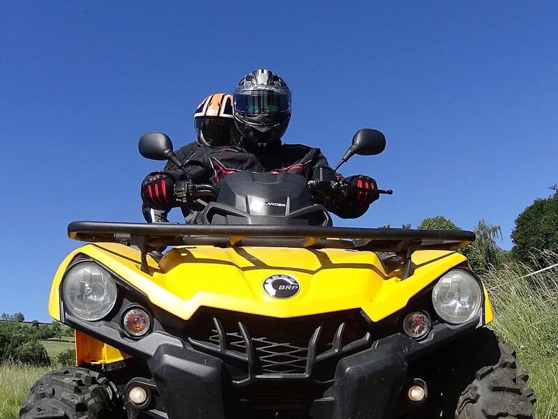 Gros plan sur un quad jaune avec deux personnes portant des casques, sous un ciel bleu clair.