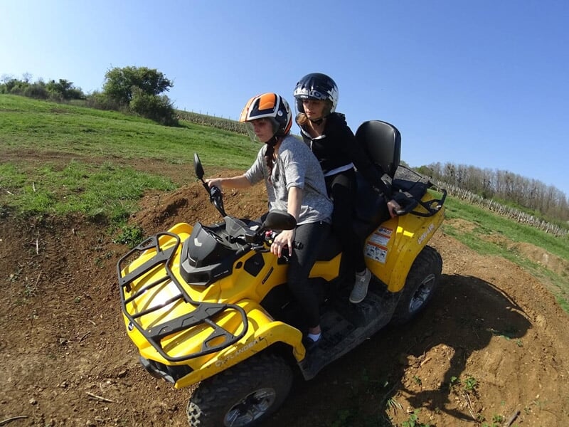 Deux personnes en quad jaune sur un terrain accidenté avec de la végétation et un ciel bleu.
