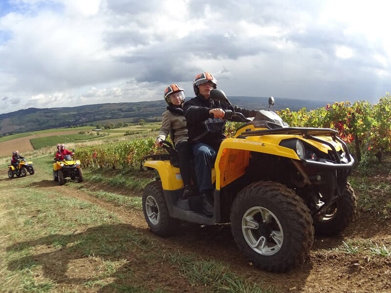 Personnes en quad jaune roulant sur un chemin dans un paysage de vignes avec un ciel nuageux.