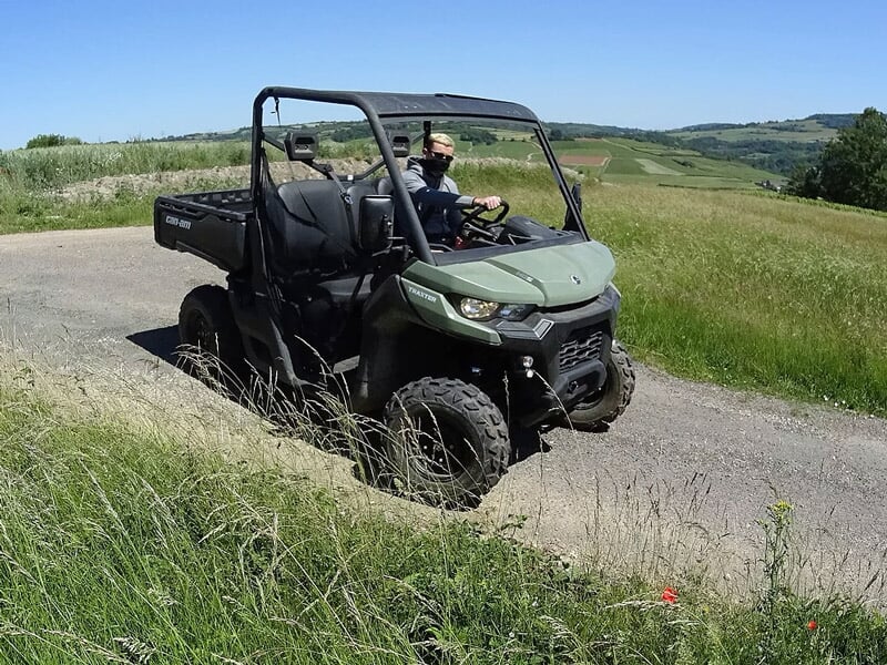 Buggy tout terrain vert avec deux personnes roulant sur une route asphaltée bordée d'herbe verte.