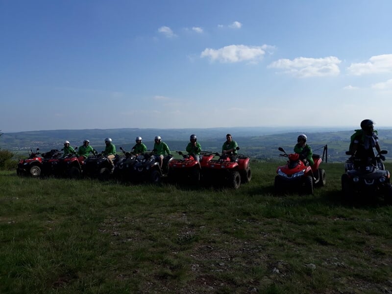 Groupe de personnes en tenue verte sur des quads alignés sur une colline avec vue panoramique sous un ciel bleu clair.