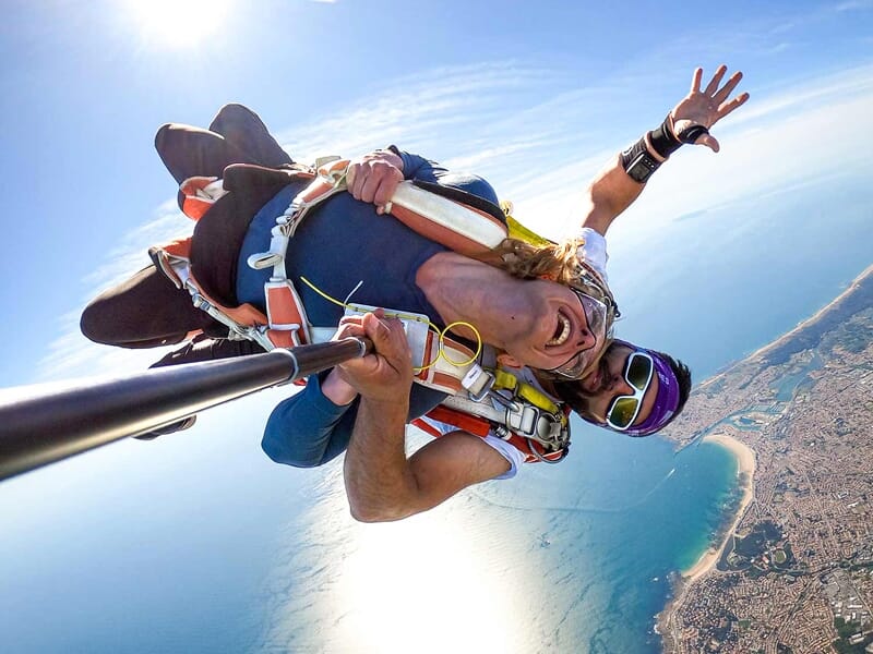 Duo en parachute tandem s'éloignant de la caméra, vue aérienne de la côte, ciel bleu clair