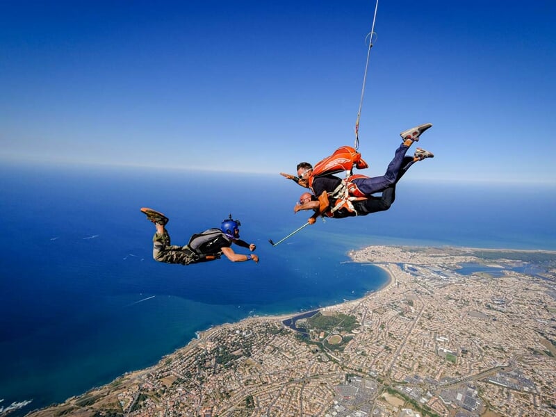 deux parachutistes en tandem sont en chute libre au-dessus de la côte atlantique tandis qu'un vidéoman les filme en chute libre