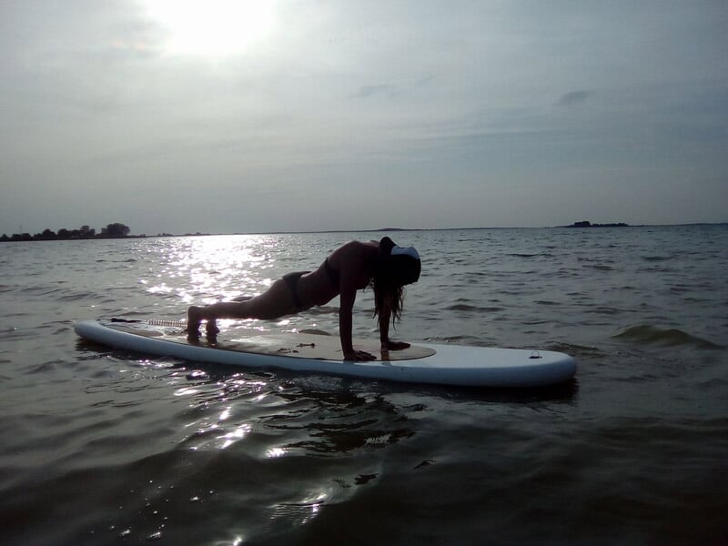Personne en équilibre sur un stand up paddle sur une eau calme au coucher du soleil.
