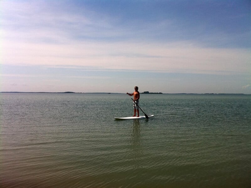 Personne pagayant sur un stand up paddle sur une grande étendue d'eau sous un ciel clair.