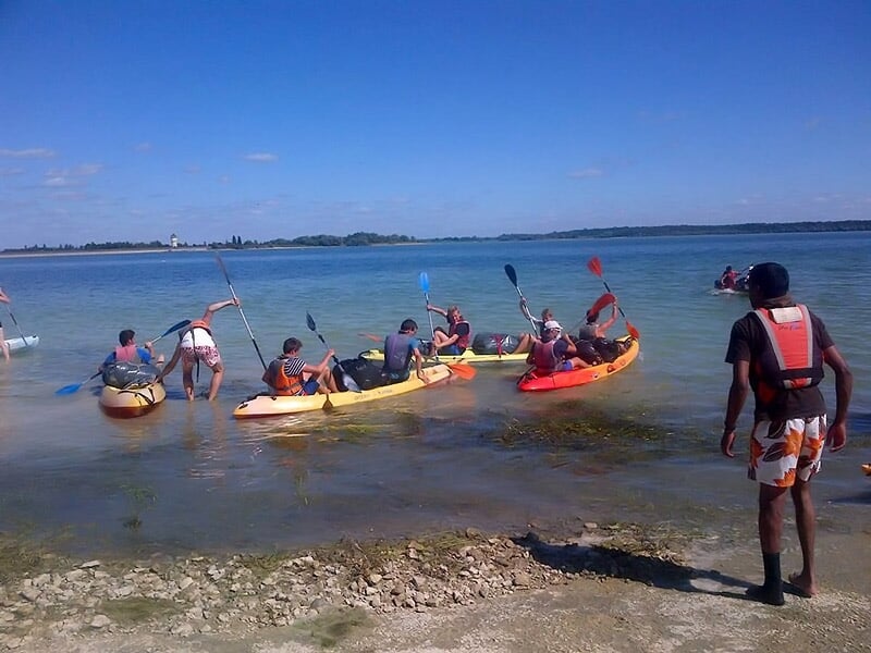 Groupe de personnes en kayak jaune et orange sur la rive d'un lac, prêtes à partir.