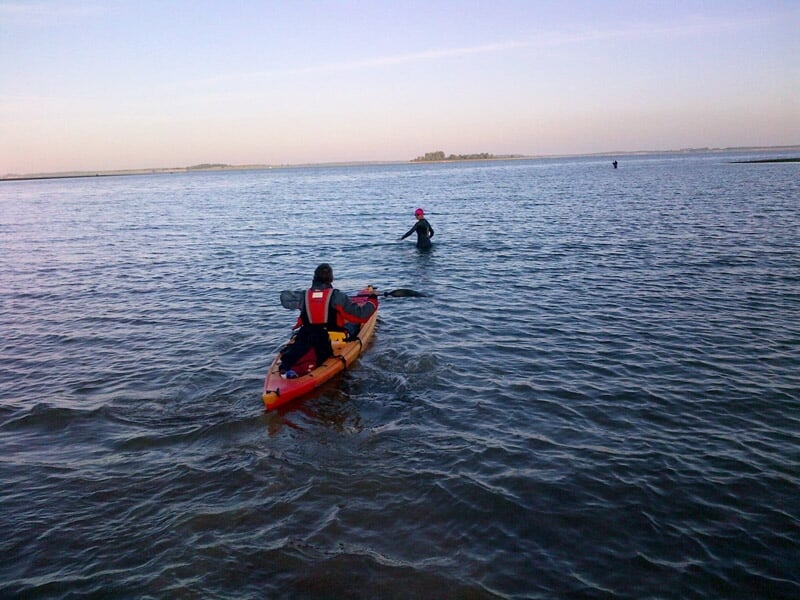 Deux personnes en kayak rouge pagayant sur un lac calme sous un ciel clair.