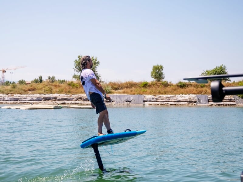 Homme debout sur une planche de foil électrique sur une eau turquoise près d'un quai.
