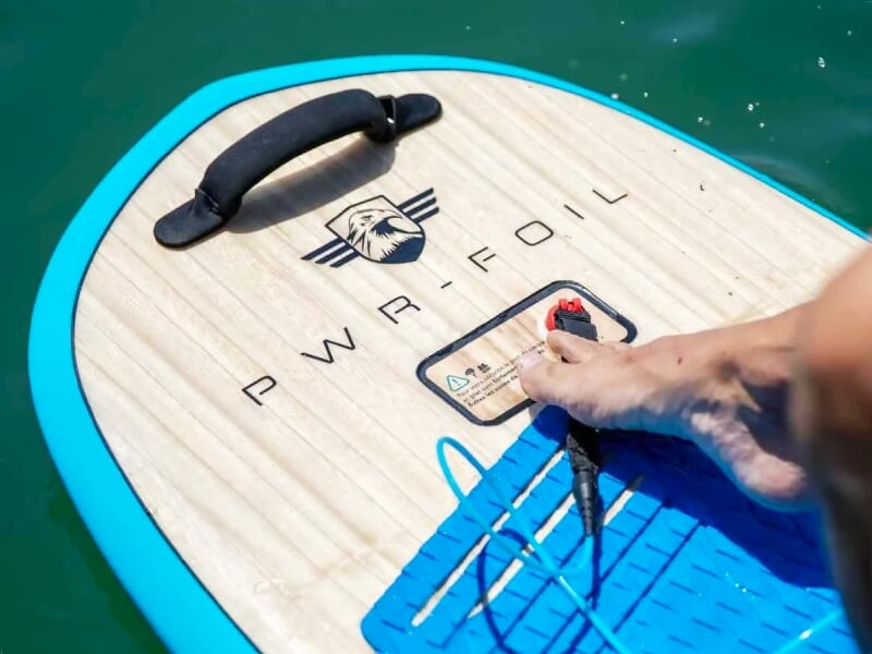 Gros plan sur une planche de foil électrique bleue avec pied et main d'un utilisateur.