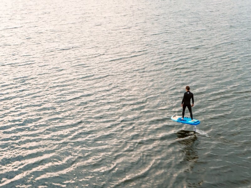 Personne en combinaison noire sur une planche de foil électrique flottant au-dessus de l'eau.
