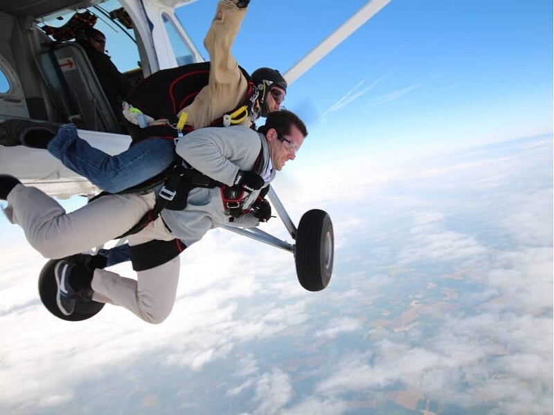 Saut en parachute depuis un petit avion, deux personnes attachées en tandem prêtes à sauter.