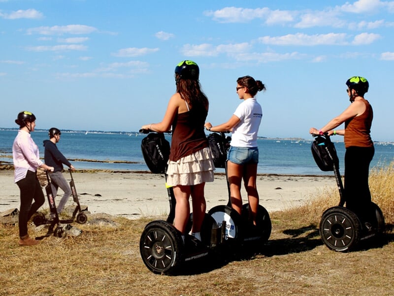 Quatre personnes en segway sur un chemin de bord de mer, sous un ciel bleu avec quelques nuages.