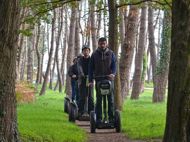Quatre personnes en segway traversant un sentier forestier entouré d'arbres verts et hauts.