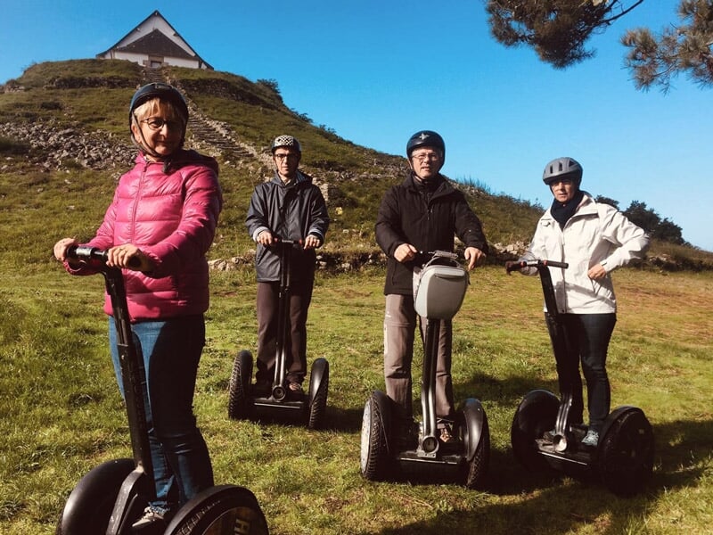 Quatre personnes en segway sur une colline herbeuse avec une petite chapelle blanche en arrière-plan.