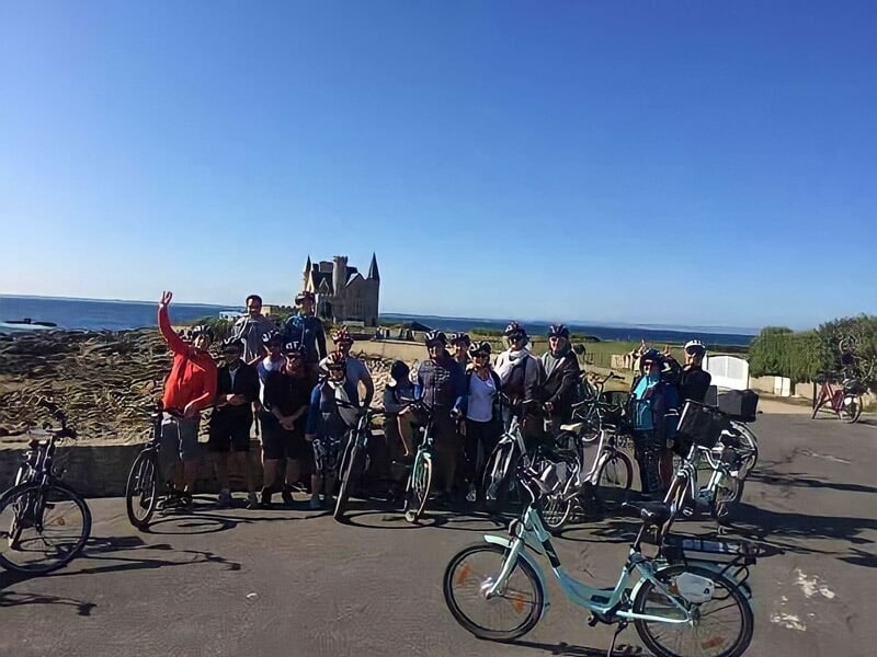 Groupe de cyclistes posant avec leurs vélos électriques sur une route côtière ensoleillée.