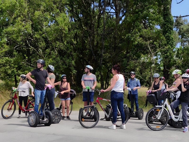 Groupe de personnes en segway et vélos électriques réunis sur une route, discutant sous un ciel clair.