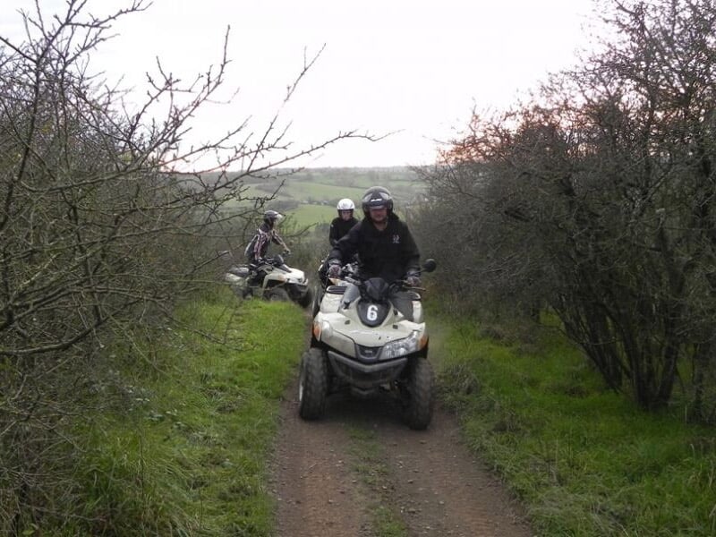 Groupe de trois personnes en quad sur un chemin étroit entouré d'arbres et de buissons en automne.