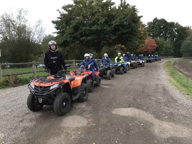 Groupe de personnes en casque sur des quads formant une file sur un chemin de campagne bordé de clôtures.