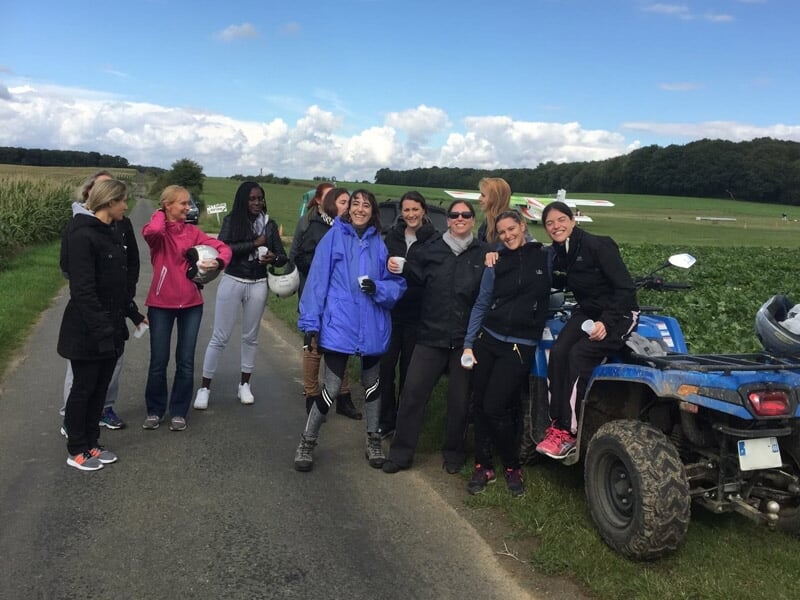 Groupe de femmes souriantes posant sur une route de campagne à côté de quads bleus et verts.