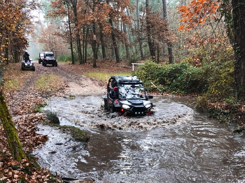 Deux quads tout-terrain roulant sur un sentier boueux en forêt avec des arbres et des feuilles.