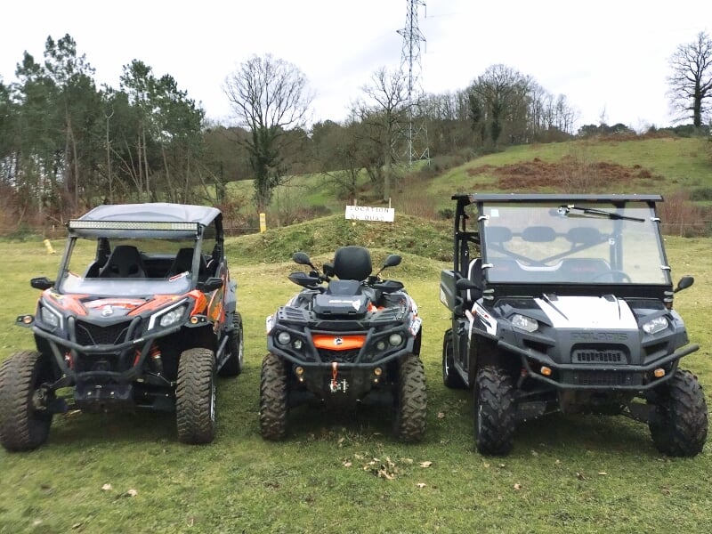 Quad noir traversant un ruisseau en forêt avec des arbres et des feuilles d'automne autour.