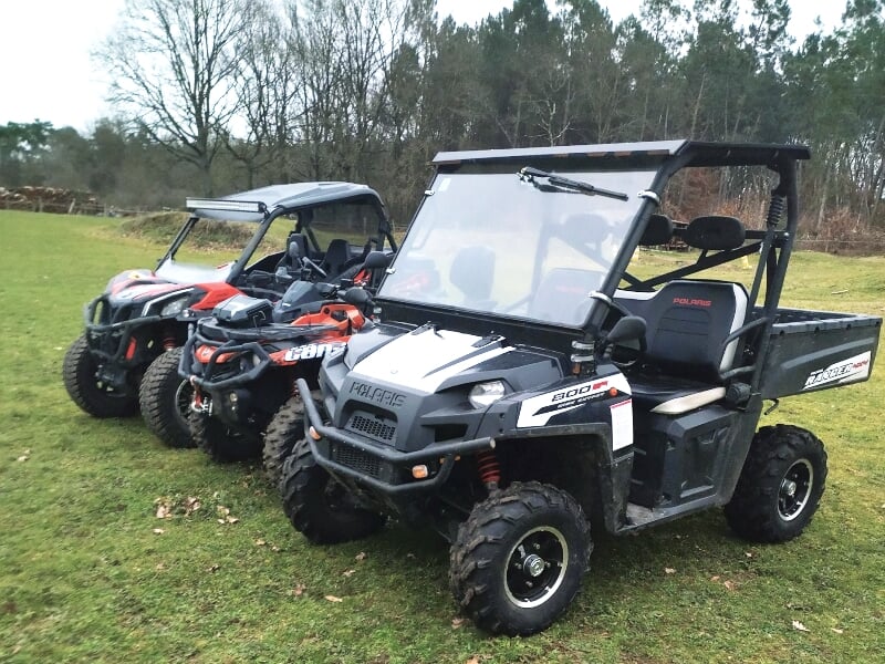 Trois quads tout-terrain stationnés sur une pelouse verte avec des collines et des arbres en arrière-plan.