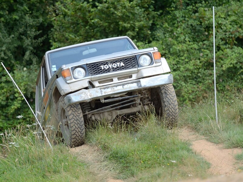 Un 4x4 Toyota blanc franchit un chemin herbeux en terrain vallonné sous un ciel dégagé.