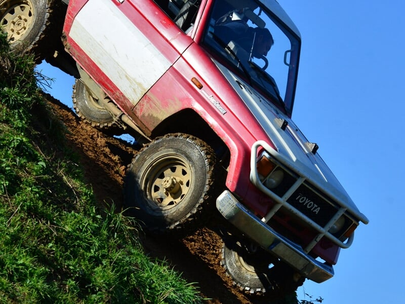 Un 4x4 rouge et blanc descend une pente boueuse en terrain escarpé avec des pneus tout-terrain.