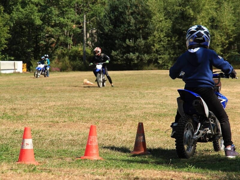 Un enfant en équipement de motocross bleu conduisant une petite moto sur un parcours herbeux balisé par des cônes de signalisation.