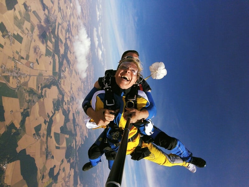 Saut en parachute en tandem avec deux personnes souriantes et paysage agricole vu d'en haut.