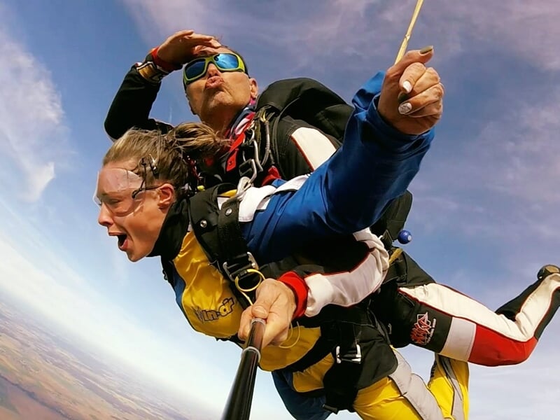 Saut en parachute avec deux personnes en tandem, ciel bleu et nuages, prise de vue en selfie.