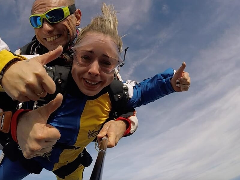 Deux parachutistes en tandem avec lunettes de protection, ciel bleu et expression de joie.