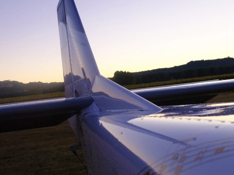 Plan rapproché sur l’empennage d’un avion scintillant au crépuscule avec collines sombres à l’horizon.