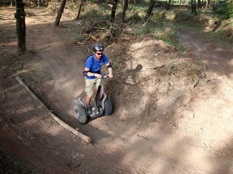 Homme en casque bleu conduisant un gyropode dans un chemin creux poussiéreux entouré d'arbres verts.