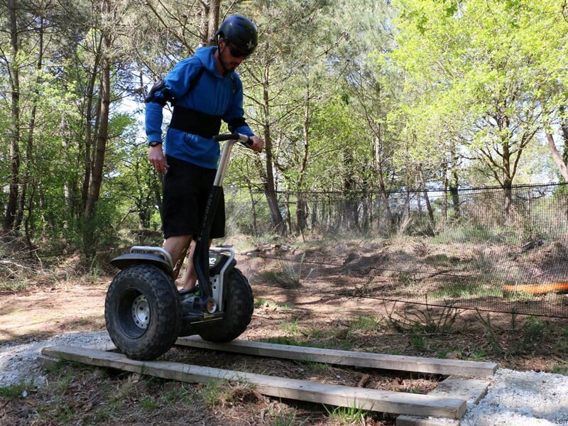 Personne en sweat bleu et casque noir sur un gyropode traversant une planche en bois posée sur des pierres.