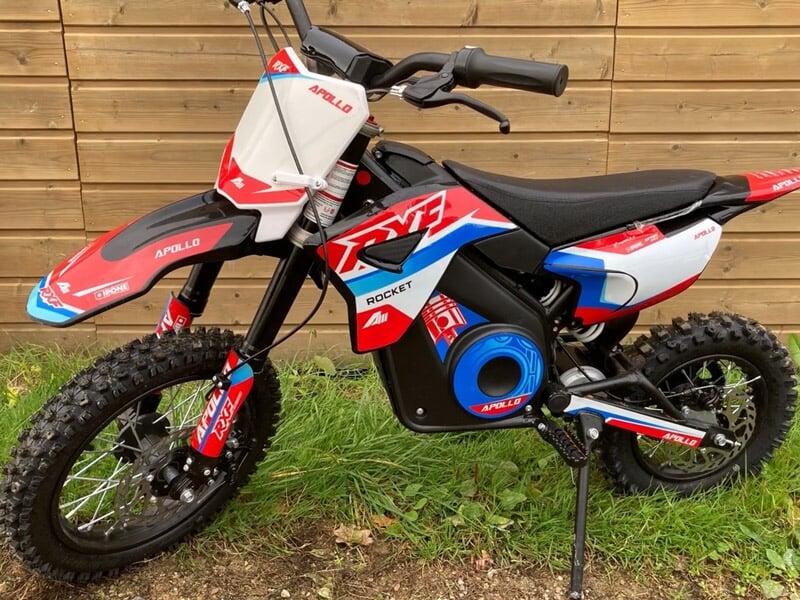 Moto électrique rouge, blanche et bleue stationnée devant un mur en bois sur une pelouse verte.