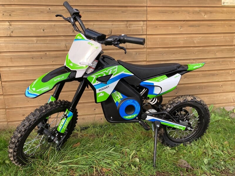 Moto électrique verte, blanche et bleue garée sur une pelouse devant un mur en bois clair.